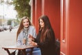 Two happy girl friends talking and drinking coffee in autumn city in cafe. Meeting of good friends, young fashionable students Royalty Free Stock Photo