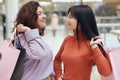 Two happy girlfriends looking smiling at each other while standing with shopping bags in mall, ladies wearing casual attire, being Royalty Free Stock Photo