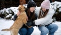 Two happy girls with dog having fun in snow at house backyard. Kids with animals, games with pets Royalty Free Stock Photo