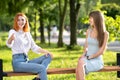 Two happy girls friends sitting on a bench outdoors in summer park chatting happily having fun Royalty Free Stock Photo