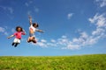 Two happy girls jump high over blue sky on lawn