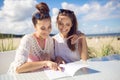 Two happy girls sitting at cafe table on beach reading menu Royalty Free Stock Photo