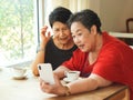 Two cheerful and healthy Asian  senior women sitting in coffee shop by the window video chatting  and laughing happily  with their Royalty Free Stock Photo