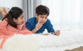 Two happy Indian brother and sister in traditional clothing lying on bed and reading book, having fun together at home. Education