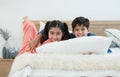 Two happy Indian brother and sister in traditional clothing lying on bed smiling and embracing each other at home