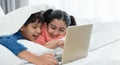 Two happy Indian brother and sister in traditional clothing lying on bed under blanket smiling, using laptop, having fun together Royalty Free Stock Photo