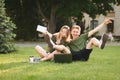 Two happy joyful students fooling around sitting on college lawn with books, laptop and take away coffee. Couple of university Royalty Free Stock Photo