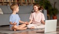 Two happy kids sitting in lotus pose and smiling while practicing yoga online Royalty Free Stock Photo