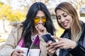 Two happy latin women friends sharing a smart phone in a coffee shop terrace looking at device in winter Royalty Free Stock Photo