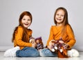 Two happy laughing kid girls friends in orange sweatshirts and blue jeans sit on floor playing with their dolls happy Royalty Free Stock Photo