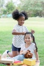 Two happy little diverse kids, African and Caucasian girls helping stick hairpin on her friend`s hair while they picnic at park Royalty Free Stock Photo