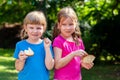 Two happy little girls eating slices of bread with butter smiling, outdoors portrait. Kids, sisters, children eating food outside Royalty Free Stock Photo