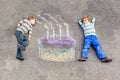 Two happy little kids having fun with big birthday cake picture drawing with colorful chalks. Creative leisure for Royalty Free Stock Photo