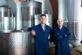 Two happy men in uniforms standing in winery fermentation compartment