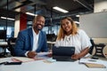 Two happy multiracial colleagues looking at camera and smiling next to digital tablet in office Royalty Free Stock Photo