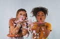 Two happy multiracial girlfriends blowing confetti at camera and having fun, enjoying birthday party