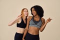 Two happy pretty diverse girls wearing sportswear having fun on beige background. Royalty Free Stock Photo