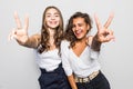Two happy pretty women posing together and showing peace gestures while looking at the camera over gray background Royalty Free Stock Photo