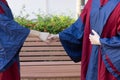 Two happy proud PhD graduated male students in Academic dress gown shake hands and congratulate each other