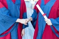 Two happy proud PhD graduated male students in Academic dress gown shake hands and congratulate each other