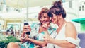 Two happy senior women friends are using a smart phone and talking while sitting in a cafe Royalty Free Stock Photo