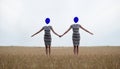 two happy sexy young women, in black and white striped dress, friends, holding hands, heads replaced by blue balloons stand hand Royalty Free Stock Photo