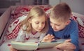 Two happy sibling children reading book in bunk bed under blanket