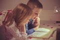 Two happy sibling children reading book in bunk bed under blanket