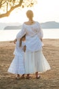 Two happy sisters, kid and teenage girl standing with their back together on the background of sea and sunset Royalty Free Stock Photo