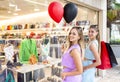 Two happy sisters standing outdoor in front of a shop window holding shopping bags and black red balloons celebrating black friday Royalty Free Stock Photo