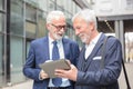 Two happy smiling senior gray haired businessmen working on a tablet