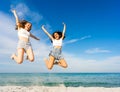 Two happy student girls jumping together looking at camera on tropical beach enjoying summer vacation in sea ocean resort. Royalty Free Stock Photo