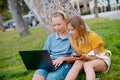 Two happy teens searching media content online in a laptop sitting on the grass in a park Royalty Free Stock Photo