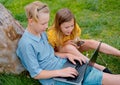 Two happy teens searching media content online in a laptop sitting on the grass in a park Royalty Free Stock Photo