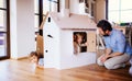 Two toddler children with father playing with paper house indoors at home.