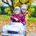 Two happy twins kids boys having fun and playing with big old toy car in autumn garden, outdoors. Brother pushing car Royalty Free Stock Photo