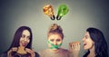 Two happy women eating hamburgers looking at stressed chubby girl with measuring tape around her mouth and junk food and vegetable Royalty Free Stock Photo