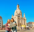 Two happy women hugging and looking at the map near main attraction of Dresden - Frauenkirche