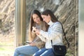 Two happy women waiting in a bus stop checking phones