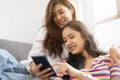 Two happy young aisan casual women having fun using smartphone on couch at home. Lesbian millennial couple. gbt