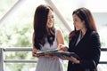 Two happy young Asian businesswomen looking into document file folder for analyzing profit or sale break even point after