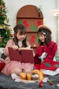 Two happy young Asian girls are having fun, enjoying reading a Christmas fairy tale story in a book Royalty Free Stock Photo