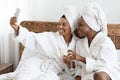 Happy ladies in bathrobes sitting on bed and taking selfie