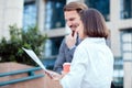 Two happy young business partners meeting in front of an office building, looking at sale charts and discussing project details Royalty Free Stock Photo