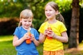 Two happy young cheerful little school age girls holding opened glass bottles full of healthy orange carrot juice fruit drink Royalty Free Stock Photo