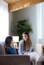 Two happy young female friends conversing in living room at home.