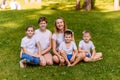 Two happy young mothers and three children in white t-shirts sit on a green lawn in the summer. Big Caucasian family on vacation. Royalty Free Stock Photo