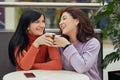 Two happy young women drinking coffee in cafe and laughing, wearing casual sweaters, telling interesting stories, haven t seen for