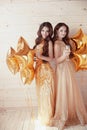 Two happy young women on party with glasses of champagne. Cheerful girls in long fashion dress by golden stars balloons over Royalty Free Stock Photo