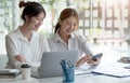 Two hardworking young women entrepreneurs working together on their laptop computers read screens with smiling faces in high